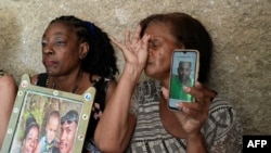 Osmara Garcia Mesa (izq.) y Amparo Rivera muestran fotos de sus hijos, desaparecidos en el mar cuando intentaban emigrar a EEUU. (Yamil Lage/AFP)